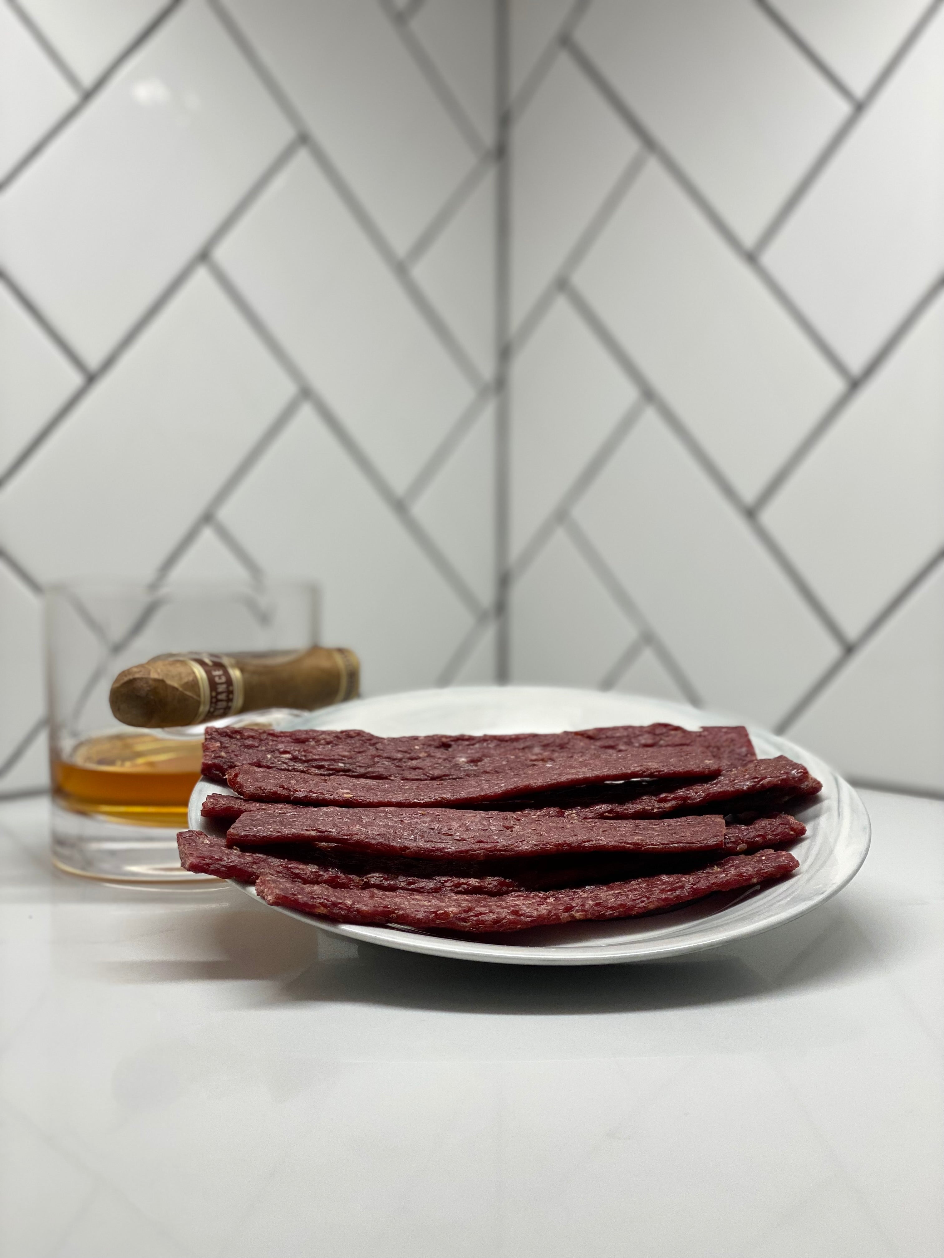 Tangy Teriyaki Beef Jerky Flats on plate with cigar in whiskey glass behind it